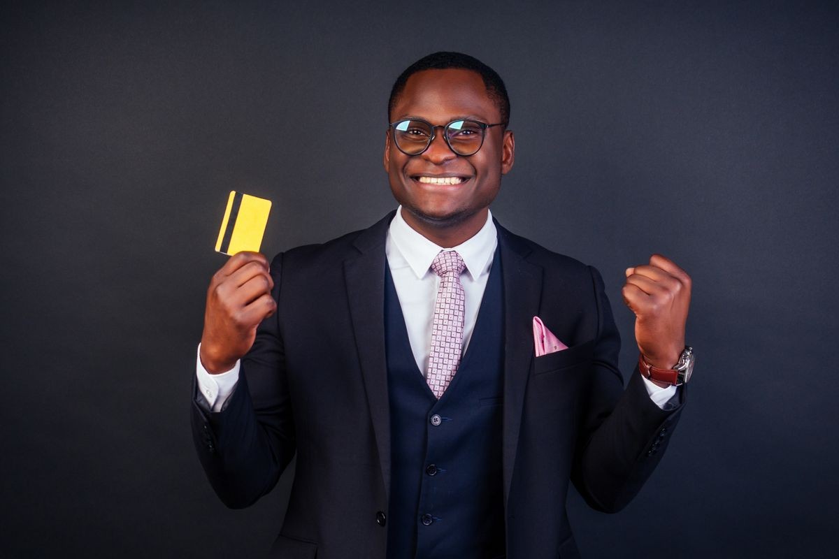 young successful businessman man in a stylish black classic suit and in cool glasses holding a yellow plastic credit card in the studio on a dark background. shopping concept black friday sale